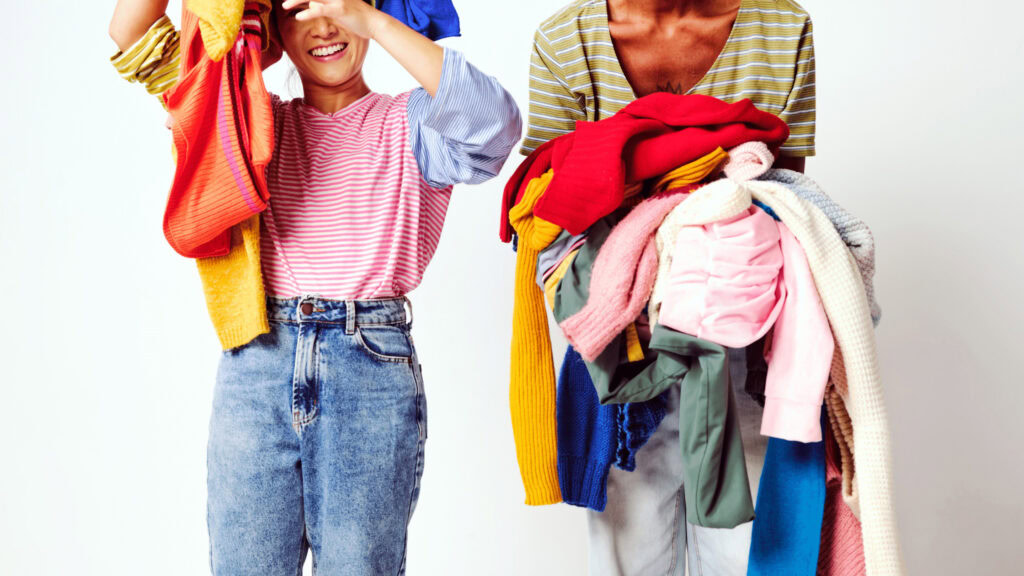Two people holding piles of clothes.